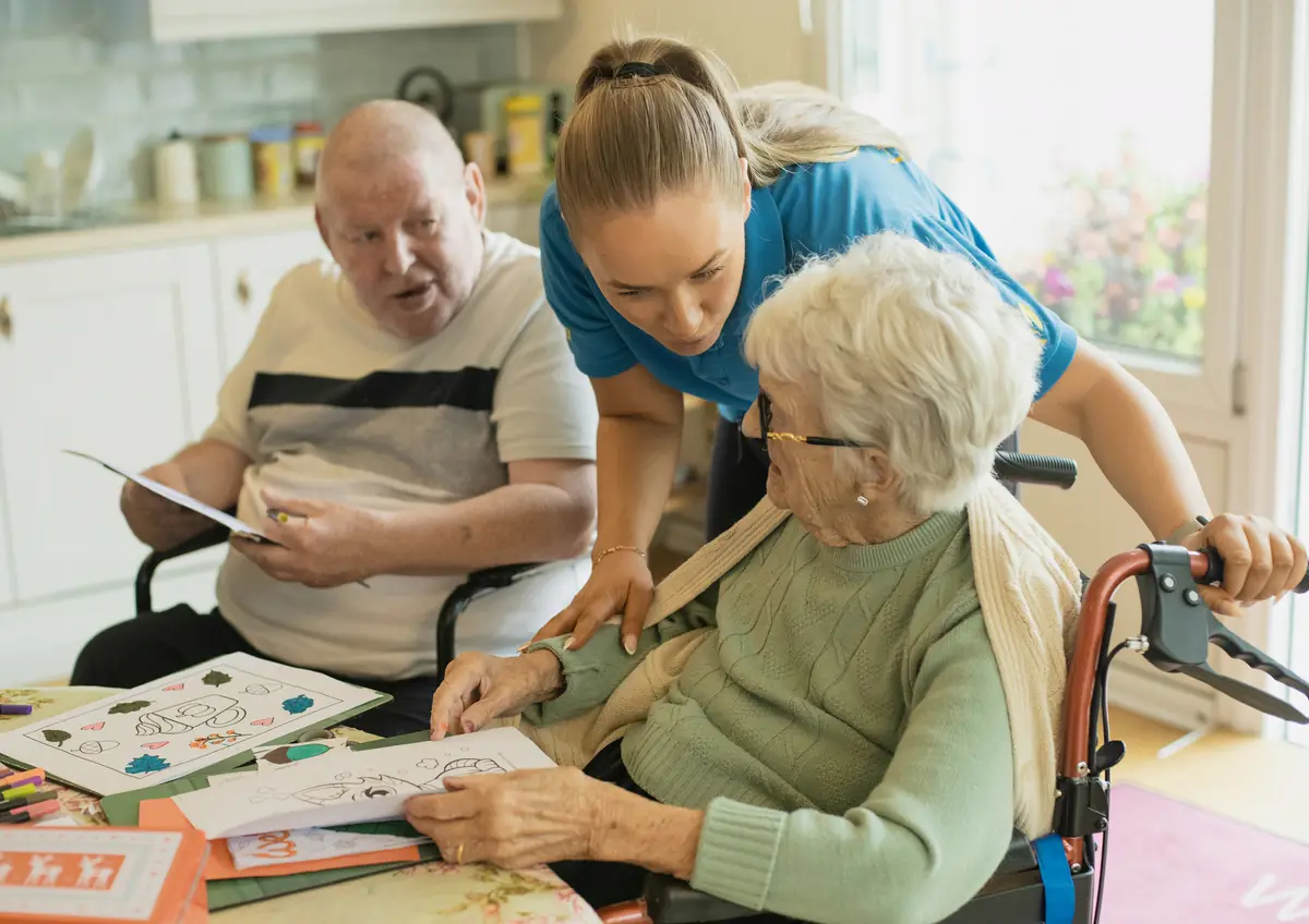 A carer helping an elderly couple with a drawing activity