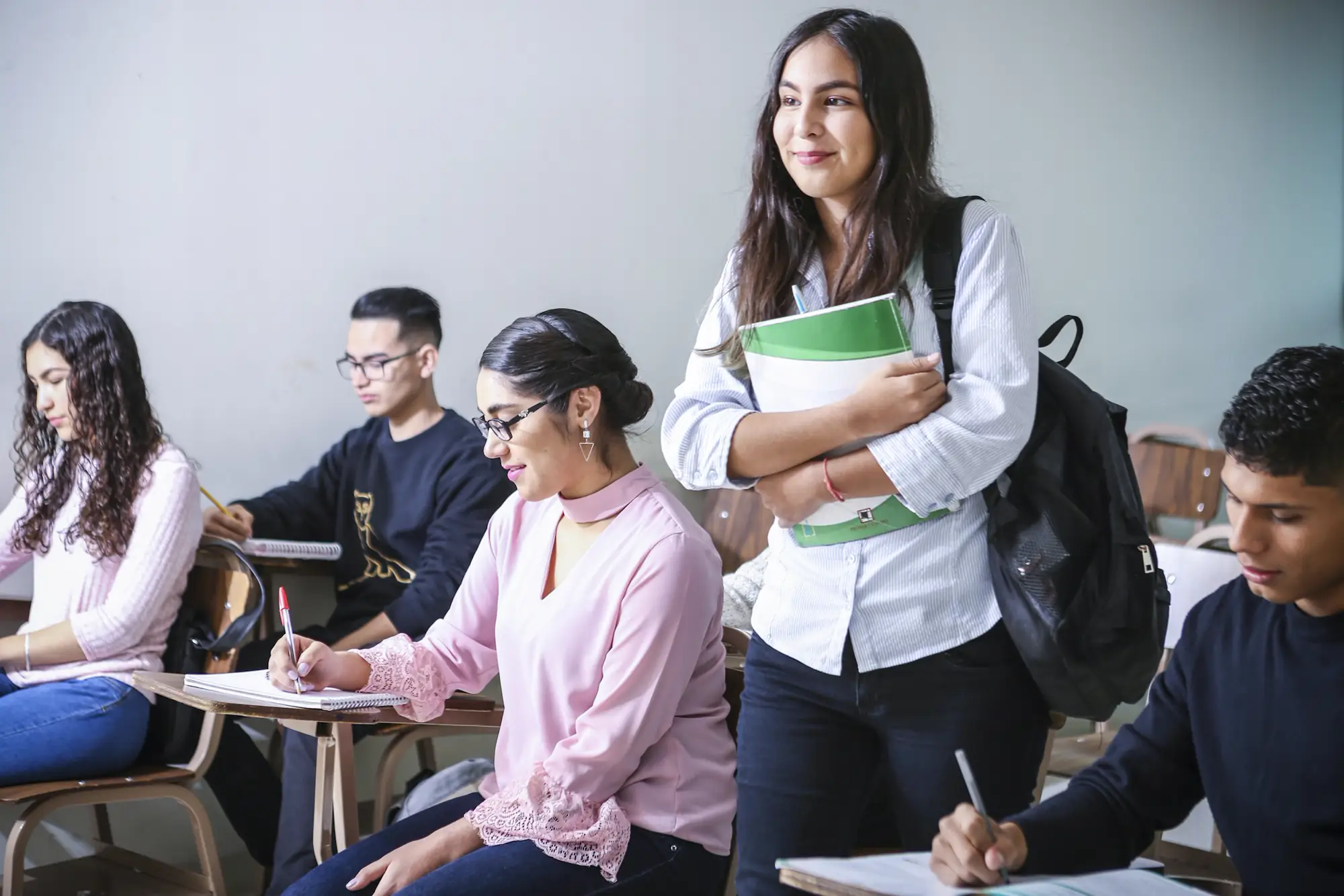 A student holding textbooks in a classroom with her classmates
